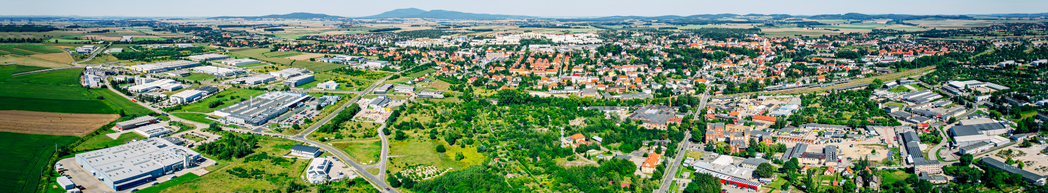 Widok z lotu ptaka na strefy aktywności gospodarcze, w oddali budynki mieszkalne i góry.