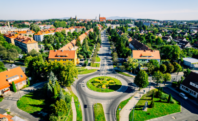 A bird's eye view of Dzierżoniów – a roundabout in the foreground, urban development surrounded by greenery and a view of the city center and hills in the distance.