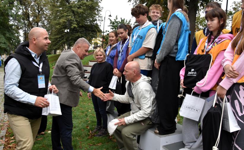 Uczestnicy Gry Terenowej na podium. Burmistrz Dzierżoniowa  gratuluje opiekunowi zwycięzkiej drużyny.