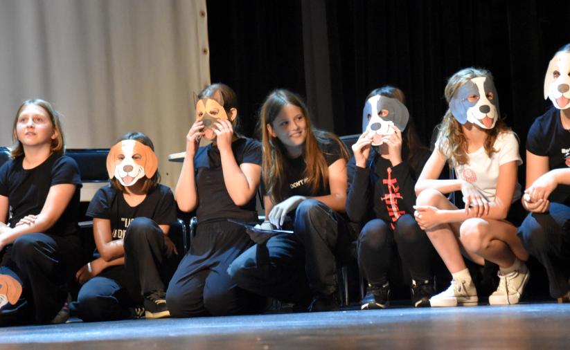 Grupa uczniów kuca na scenie z maskami psów