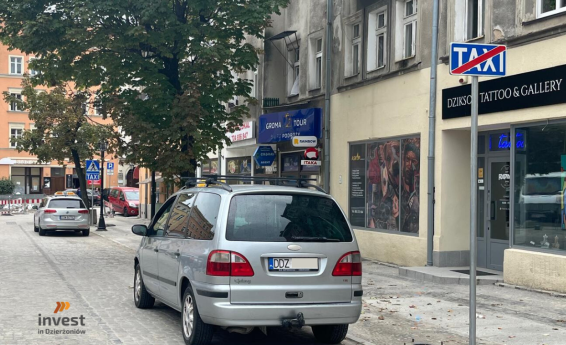 Postój Taxi. W kolejce czekają dwa auta. Logo Invest in Dzierżoniów.
