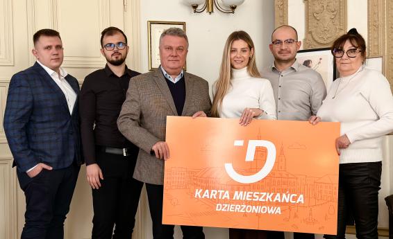 The Mayor and local entrepreneurs pose for a photo in the mayor’s office holding a board reading “Dzierżoniów Resident Card.”