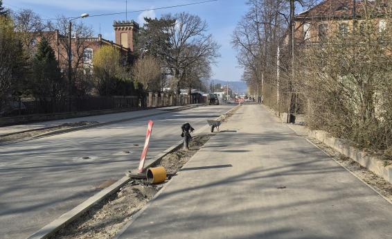 Street under renovation with temporary traffic signs and barriers, residential buildings and vehicles in the background.