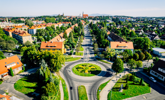 Panorama Dzierżoniowa z lotu ptaka – rondo na pierwszym planie, zabudowa miejska otoczona zielenią oraz widok na centrum miasta i wzgórza w oddali.